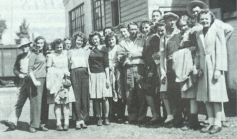 Historical group photo of men and women in vintage clothing outside a building.