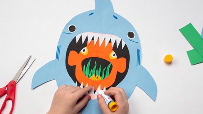 Child crafting a paper shark with vibrant colors and glue stick on table